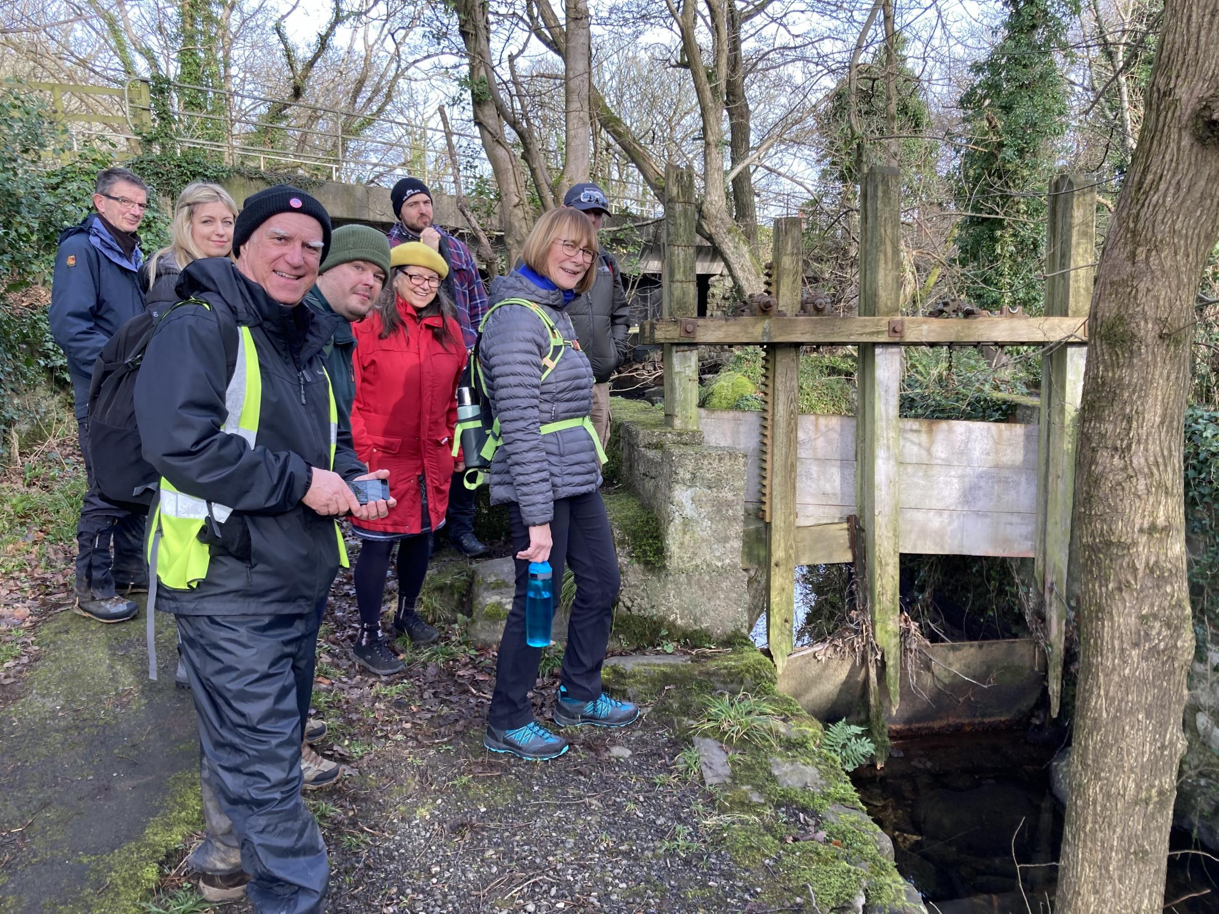 History walk with Rhys Mwyn, discovering Caernarfon\s boundary stories. Walkers are seen looking at the old mill sluice gate at the end of Seiont Mill Road